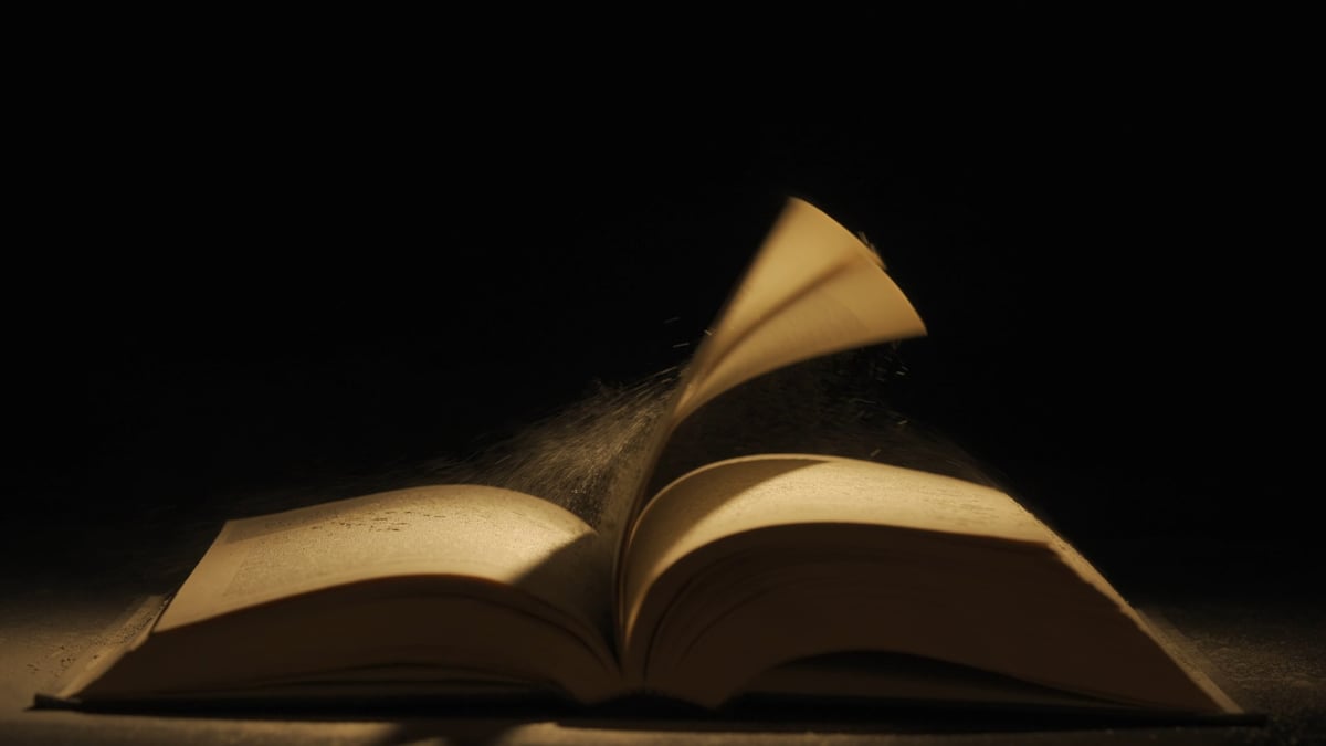 An open vintage hardcover book with a page turning in warm light