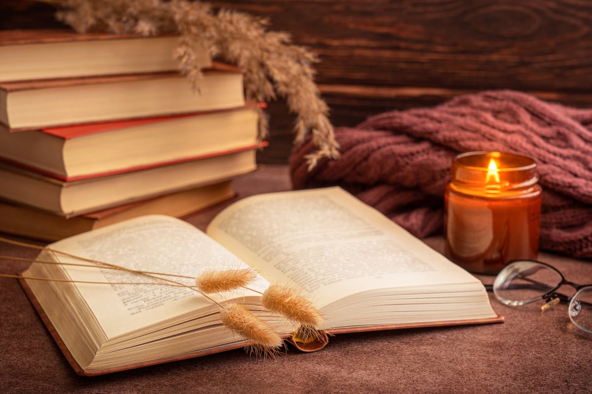 An open book with dried plants, glasses and candlelight on a warm wooden table